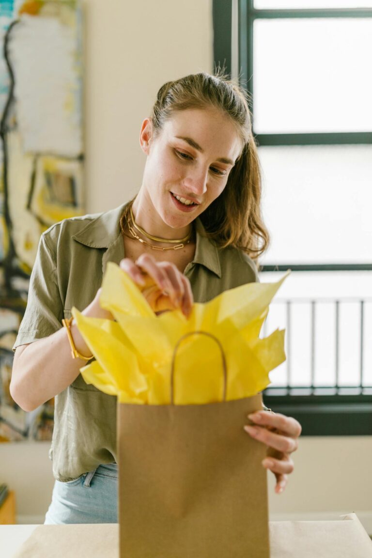 Adult woman showcasing her craft business skills by packing a gift with yellow tissue paper.