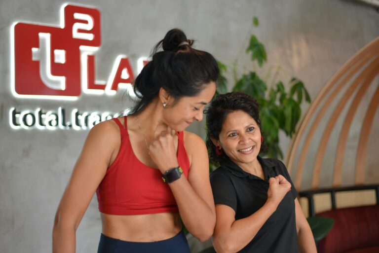 Two women flexing and smiling at a gym in Singapore, embracing fitness and positivity.